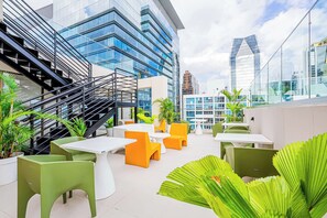 An outdoor seating area with tables and chairs, surrounded by potted plants and modern buildings in the background. - w* | Upscale 1BR in Obarrio w/ AC (Panamá)