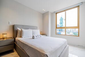 Et moderne hotelværelse med en stor seng, et natbord, en lampe og et vindue med udsigt over bybilledet.