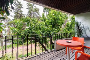 Ein Balkon mit Tisch und Stühlen, der auf einen Garten mit Bäumen und einem Pfad blickt.
