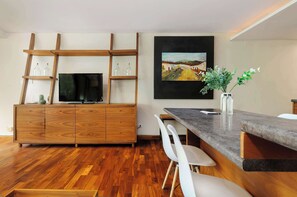 Eine moderne Küche mit einem Holzkorpus, einem Flachbildfernseher und einem Essbereich mit Marmorplatte und weißen Stühlen.