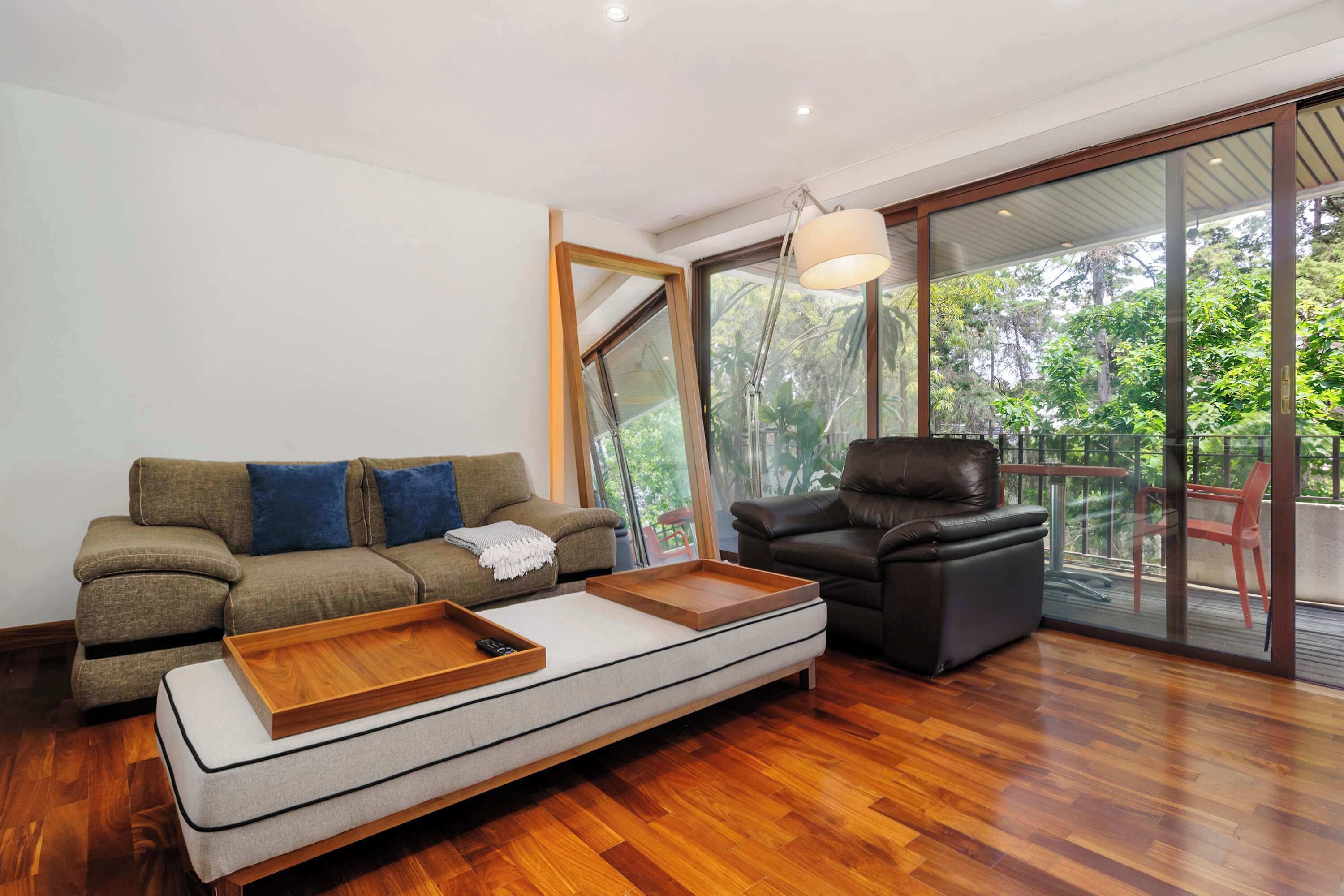 A modern living room with a sofa, a leather chair, a wooden coffee table, and a large glass door leading to an outdoor area.