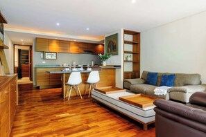 Un salon moderne avec un canapé, une table basse et un coin repas comprenant des chaises, et une cuisine en arrière-plan.
