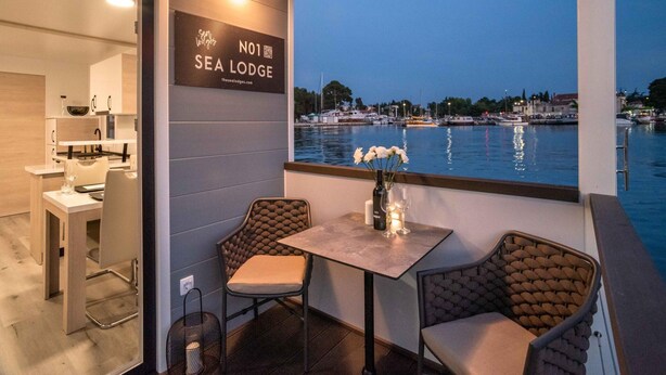 Een eethoek met uitzicht op het water, een bordje met Sea Lodge en een tafel met stoelen.