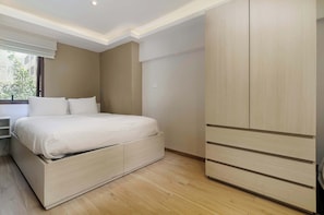 Ein Schlafzimmer mit einem Bett, einem Kleiderschrank, einem Nachttisch und einem Fenster mit Blick auf Gebäude.
