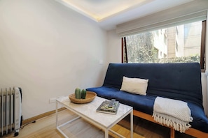 Ein kleines Wohnzimmer mit einem blauen Sofa, einem weißen Couchtisch und einer Heizung.