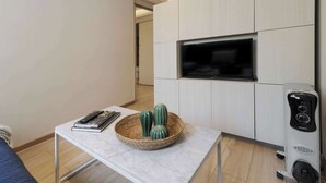 A modern living room with a flat-screen TV mounted on a wall, a small table with a basket of decorative items, and a standing heater. - w* | Charming & Cozy 1BR in Prime Polanco (Ciudad de México)