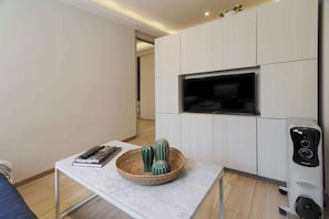 Ein modernes Wohnzimmer mit einem an der Wand befestigten Flachbildfernseher, einem kleinen Tisch mit einer Korb-Dekoration und einem Standheizkörper.