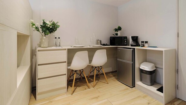 A compact kitchen with a built-in microwave, a coffee maker, and a small refrigerator. There are two white chairs and a plant on the counter. - w* | Enchanting 1BR in Prime Polanco (Ciudad de México)