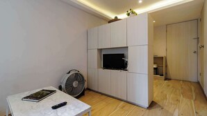A modern living room with a flat-screen TV mounted on a light-colored cabinet, a standing fan, a marble table with a book and remote, and a wooden floor. - w* | Enchanting 1BR in Prime Polanco (Ciudad de México)
