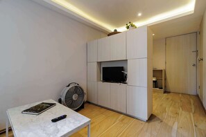 A modern living room with a flat-screen TV mounted on a light-colored cabinet, a standing fan, a marble table with a book and remote, and a wooden floor. - w* | Enchanting 1BR in Prime Polanco (Ciudad de México)