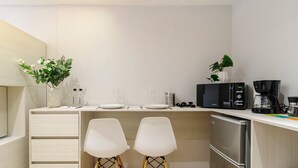 A compact kitchen with a white countertop, two white chairs, a coffee maker, and a refrigerator. - w* | Enchanting 1BR in Prime Polanco (Ciudad de México)