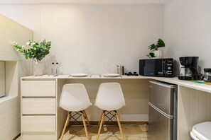 A compact kitchen with a white countertop, two white chairs, a coffee maker, and a refrigerator. - w* | Enchanting 1BR in Prime Polanco (Ciudad de México)