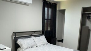 A bedroom with a bed, a nightstand, an air conditioning unit, a window with curtains, and a wardrobe. - Cozy 1-bedroom apartment in marvelous Odessa with AC (Odessa)