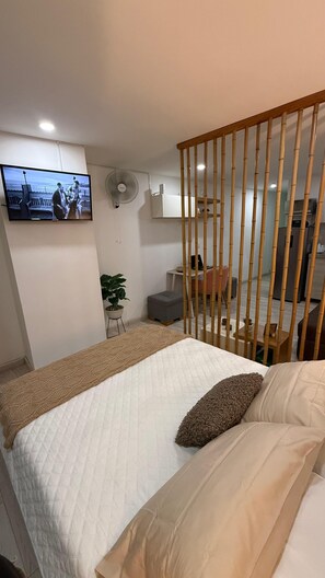 A bedroom with a bed, a television mounted on the wall, a desk with a chair, and a bamboo partition. - "A Modern Retreat in the Heart of Quindío – VENTOLOFT" (Armenia)