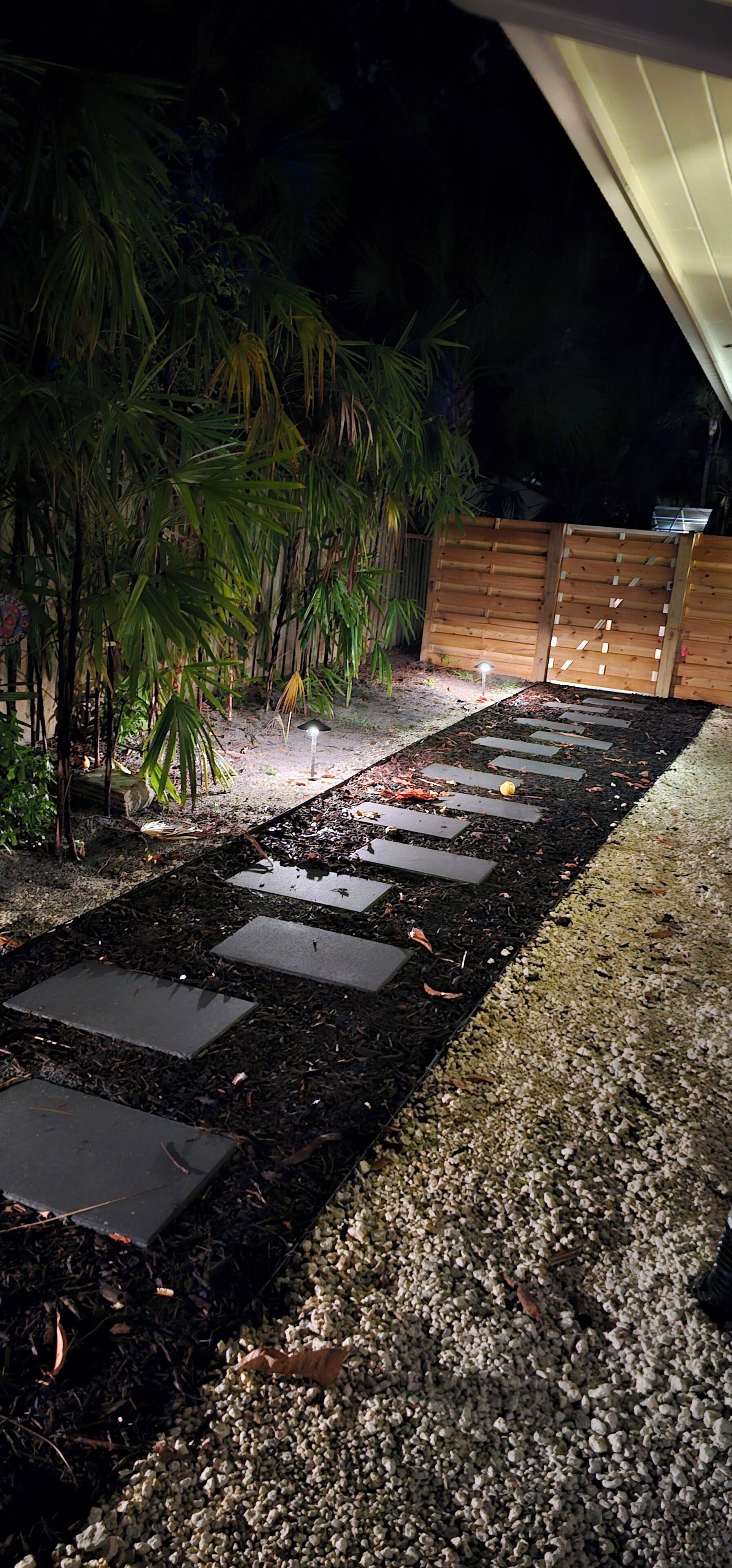 Un sendero en un jardín con piedras para pisar, rodeado de plantas y una cerca de madera.