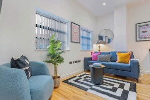 Ein Wohnzimmer mit einem blauen Sofa, einem runden Couchtisch, einem Blumentopf und einem schwarz-weißen Teppich.