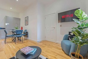 Ein modernes Wohnzimmer mit Essbereich, einem an der Wand montierten Flachbildfernseher und einer Topfpflanze.