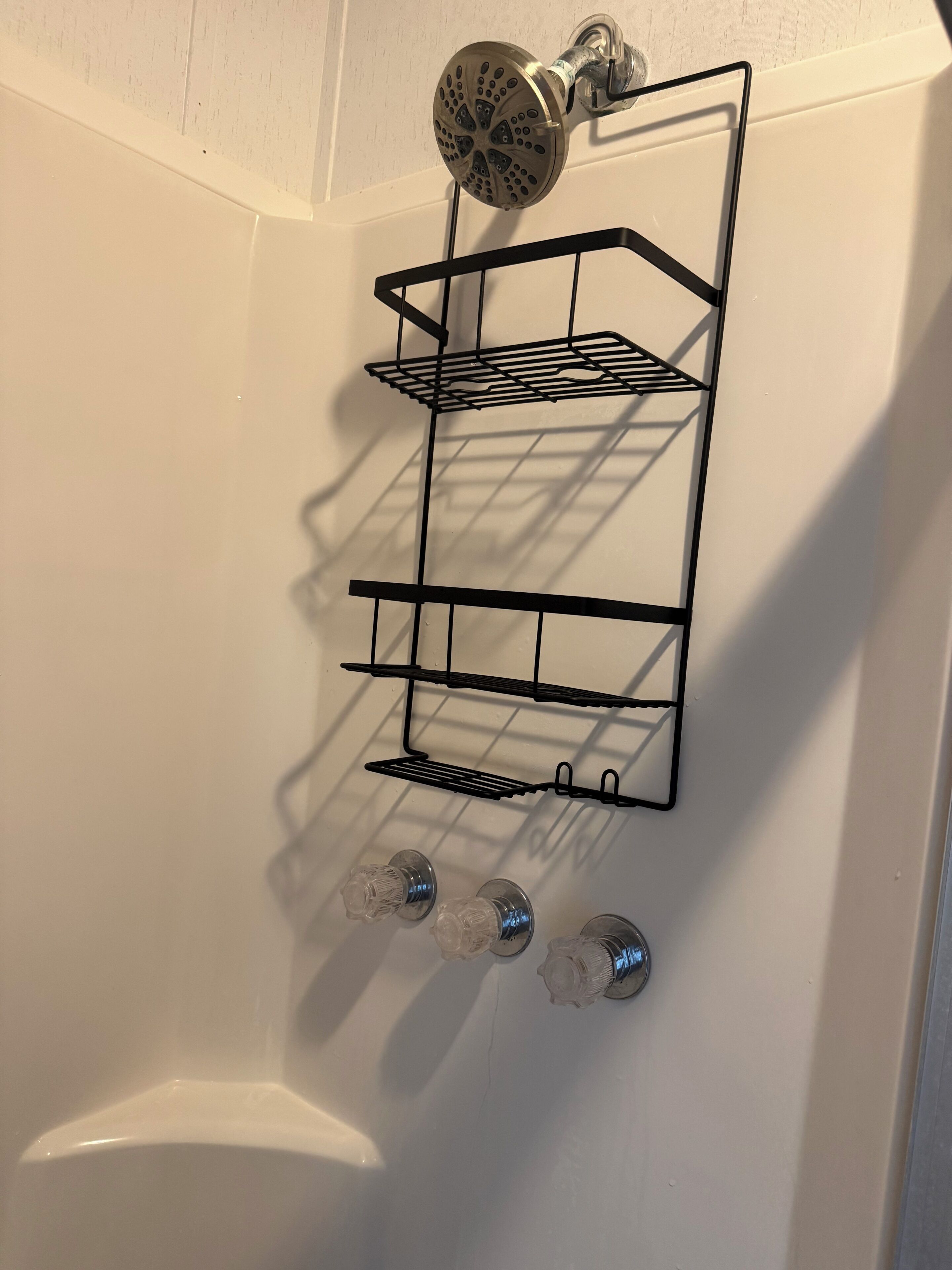 A shower with a black metal shelf holding three clear glass bottles.