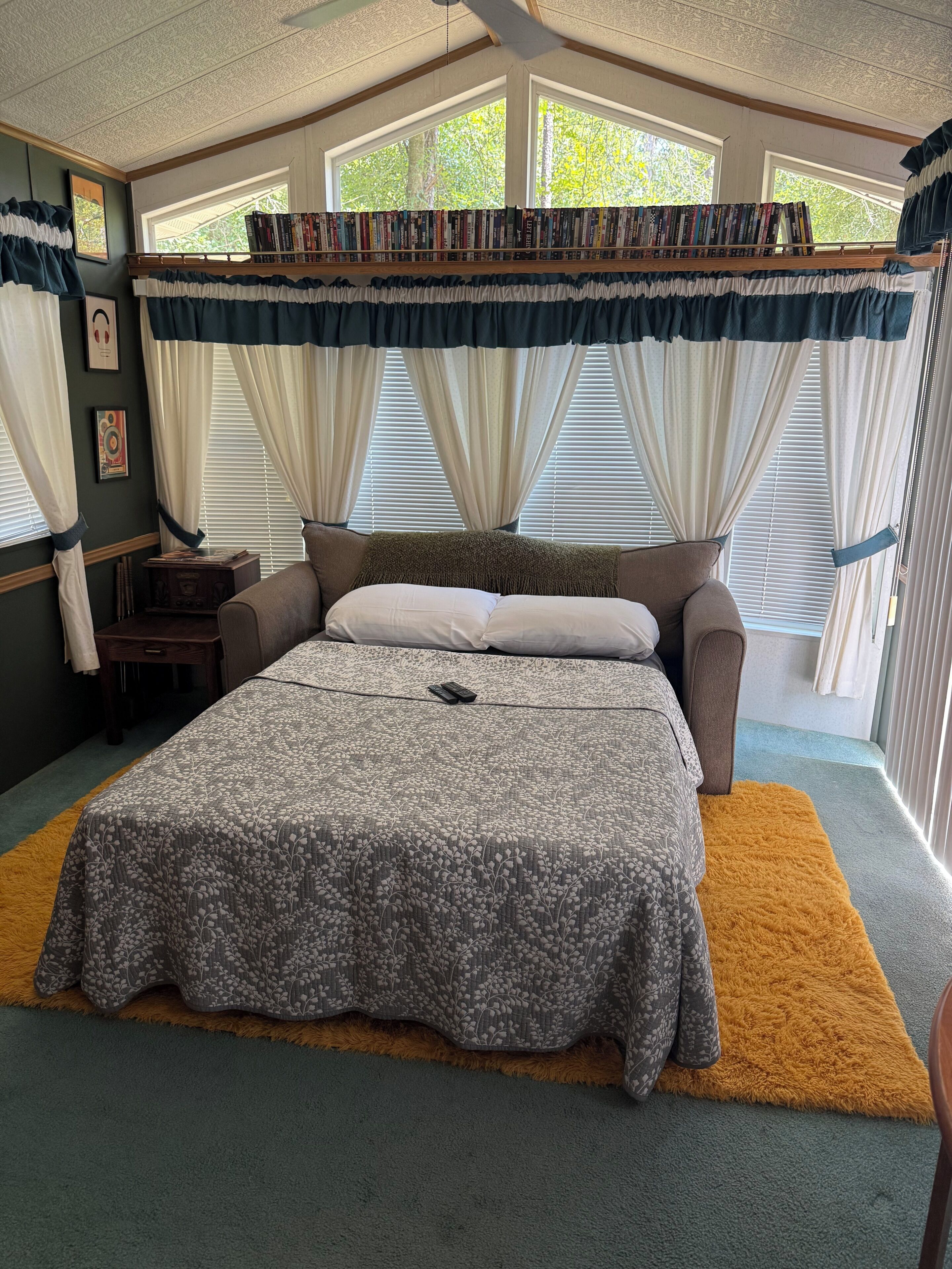 A bedroom with a large bed, a bookshelf, and a window with curtains.