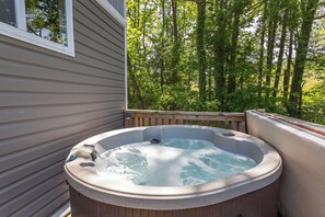 Ein Whirlpool auf einer Holzterrasse mit Blick auf einen Wald.