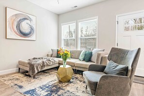 A living room with a sofa, armchair, and a coffee table with a vase of flowers. - Asheville Oasis! 3BR home w/hot tub, fire pit, & game room only 6M from downtown (Asheville)