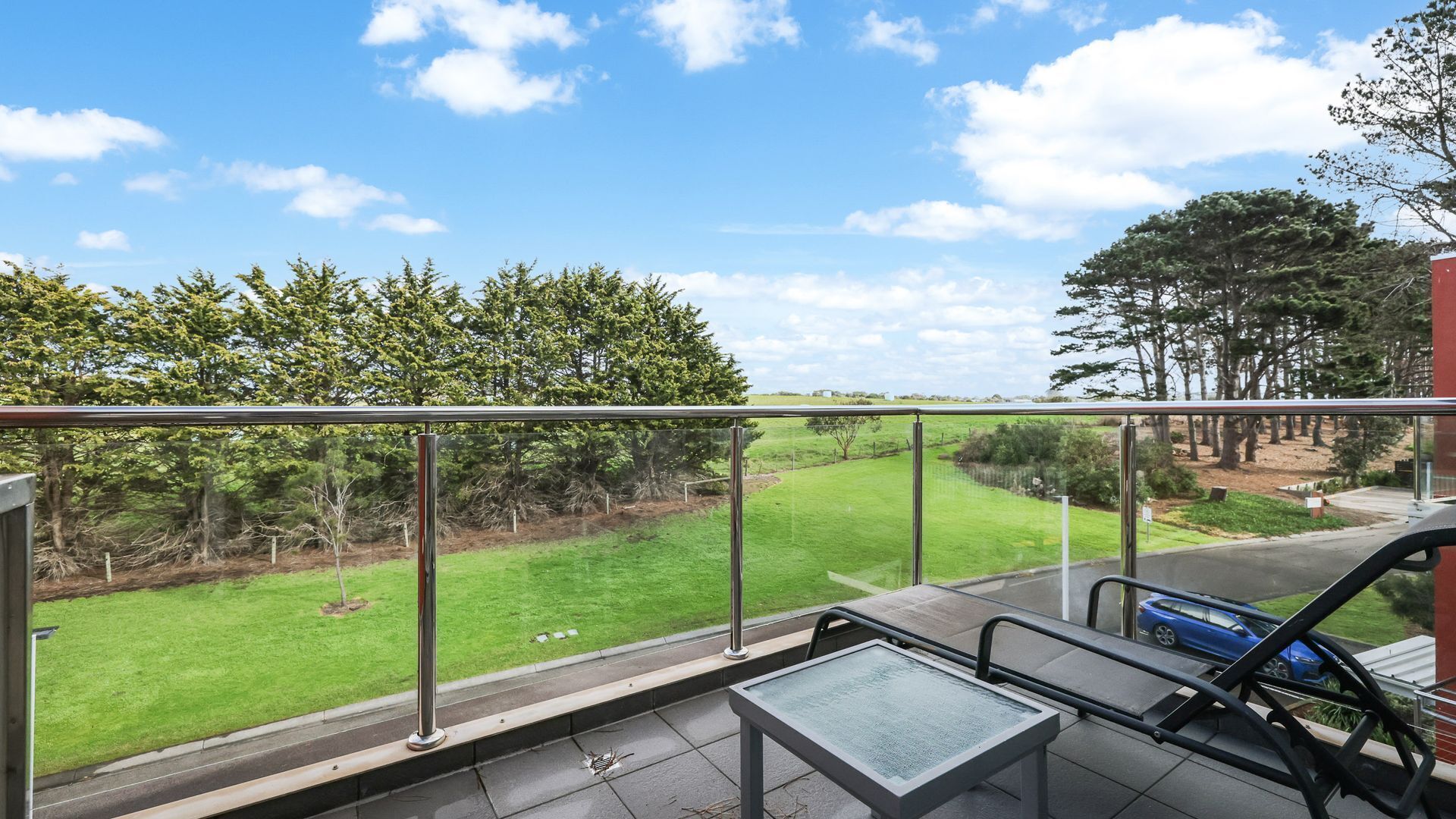 A balcony with a glass railing overlooking a grassy area and trees.