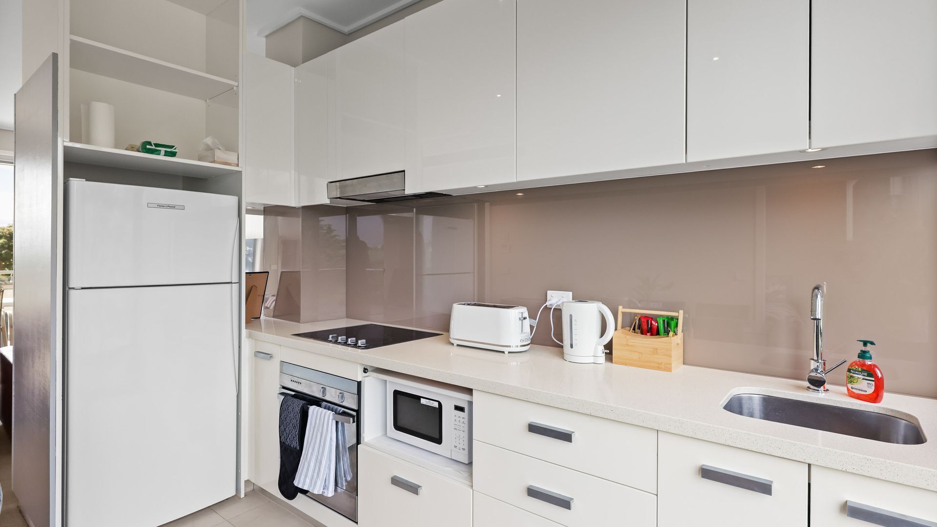 A modern kitchen with white cabinets, a built-in oven, a microwave, a toaster, and a sink.