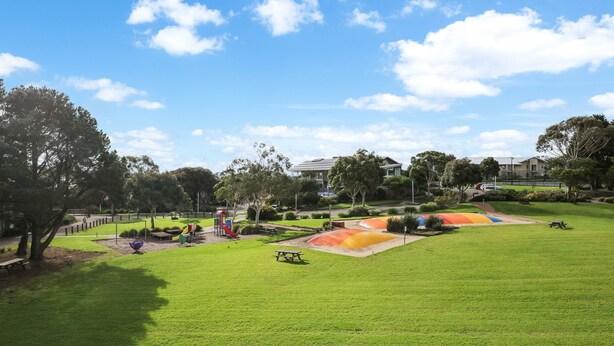 A park with green grass, playground equipment, picnic tables, and trees.
