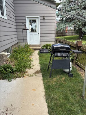 A backyard with a grill, a pathway, and a house with a white door.
