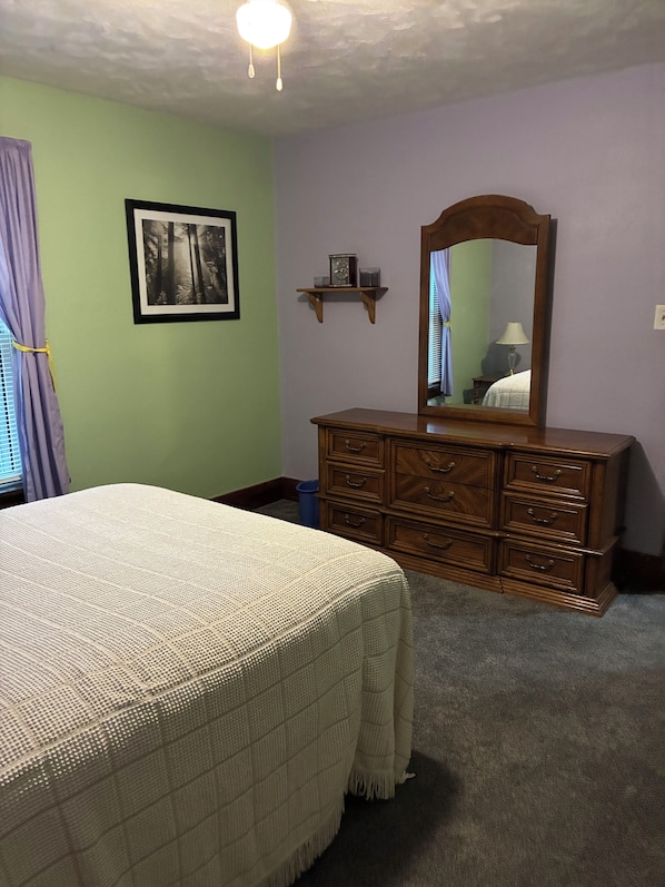 A bedroom with a bed, dresser, mirror, and a wall-mounted shelf.