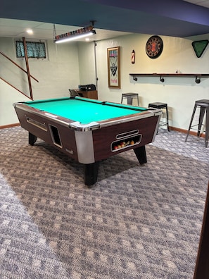 A pool table with a green felt surface, a cue stick, and a set of pool balls.