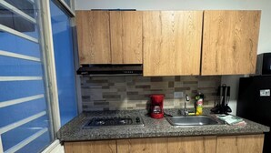 Een kleine keuken met houten kastjes, een gasfornuis, een spoelbak en een koelkast.
