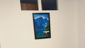 Een kamer met een houten bureau, een witte stoel, een kleine potplant en een lijst met een berglandschap.