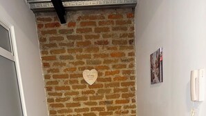 Een kamer met een bakstenen muur, een donkergrijze bank met kussens, een wit wandtelefoon en een klein, ingelijst fotootje.