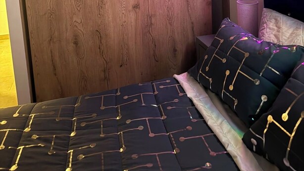 Een slaapkamer met een houten hoofdeinde, een bed met beddengoed met een patroon, en een neonlamp aan de muur.