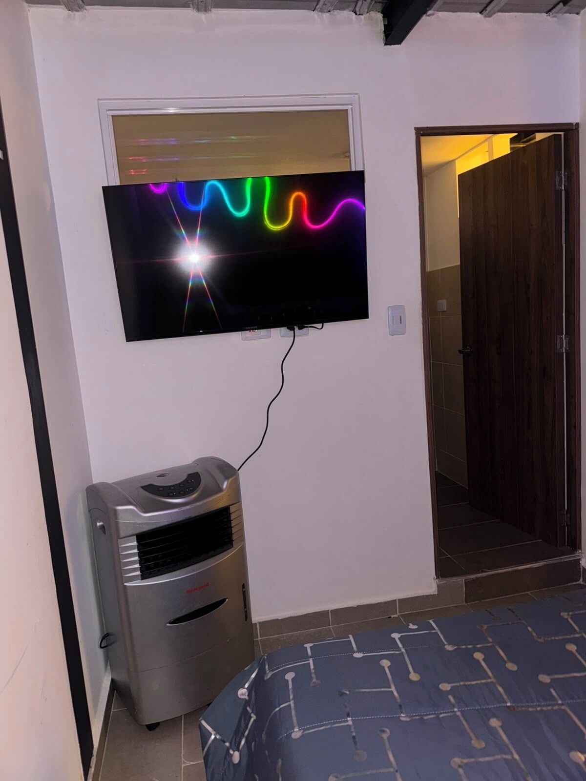 A room with a television mounted on the wall, a heater, and a bed with a patterned bedspread.