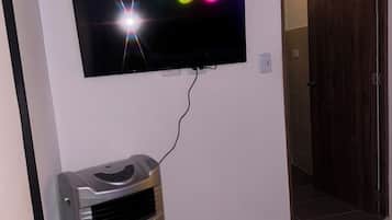A room with a television mounted on the wall, a heater, and a bed with a patterned bedspread.