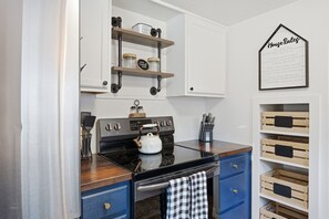 A kitchen with a stove, oven, and cabinets. There is a kettle on the stove, and a wall-mounted sign with home rules. - Charming Farmhouse Retreat (Salem)