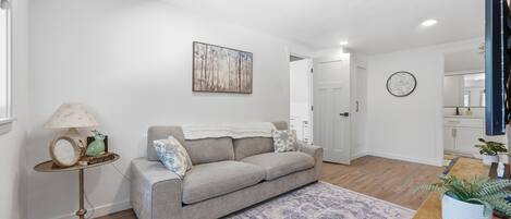 A modern living room with a grey sofa, a patterned rug, a lamp, and a painting on the wall.