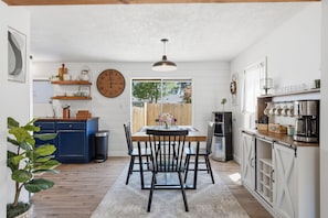 A kitchen with a dining table, chairs, a clock, and a coffee bar.