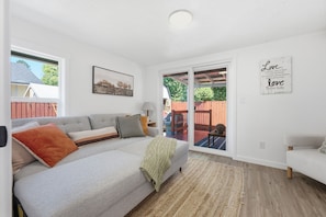 A living room with a grey sofa, a wooden floor, a large window, and a view of a backyard.