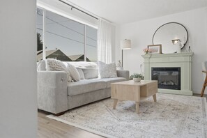 A modern living room with a grey sofa, a wooden coffee table, a fireplace, and a large window. - Charming Farmhouse Retreat (Salem)