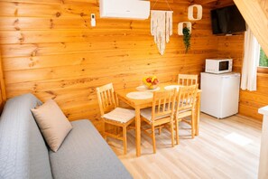 A wooden cabin interior with a dining table, chairs, a sofa, a TV, and a microwave. - Holiday Homes for 5 People Near the sea (Kamien Pomorski)