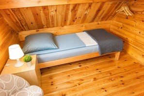 Eine kleine Holzhütte mit einem Einzelbett, einem Nachttisch mit Lampe und einer kleinen Pflanze.