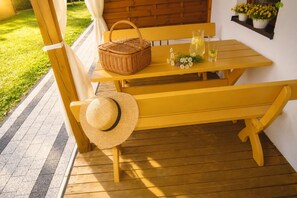 Ein Holzbänkchen und Tisch auf einer Veranda, ergänzt durch einen Korbwannen und einen Strohhut.