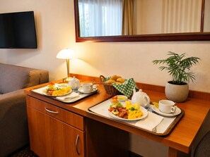 Ein Hotelzimmer mit Frühstückstisch, Fernseher, Lampe und einem Blumentopf.