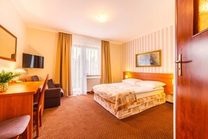 Ein Hotelzimmer mit einem Bett, einem Schreibtisch mit Stuhl, einem Fernseher und einem Fenster mit Vorhängen.