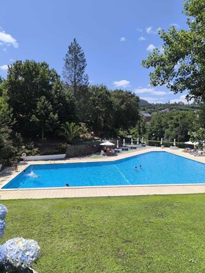 Piscina rectangular con solárium de azulejos, rodeada de césped y árboles.