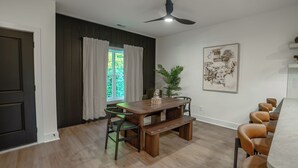 Zona pranzo con tavolo in legno, sedie, ventilatore a soffitto e finestra con tende.