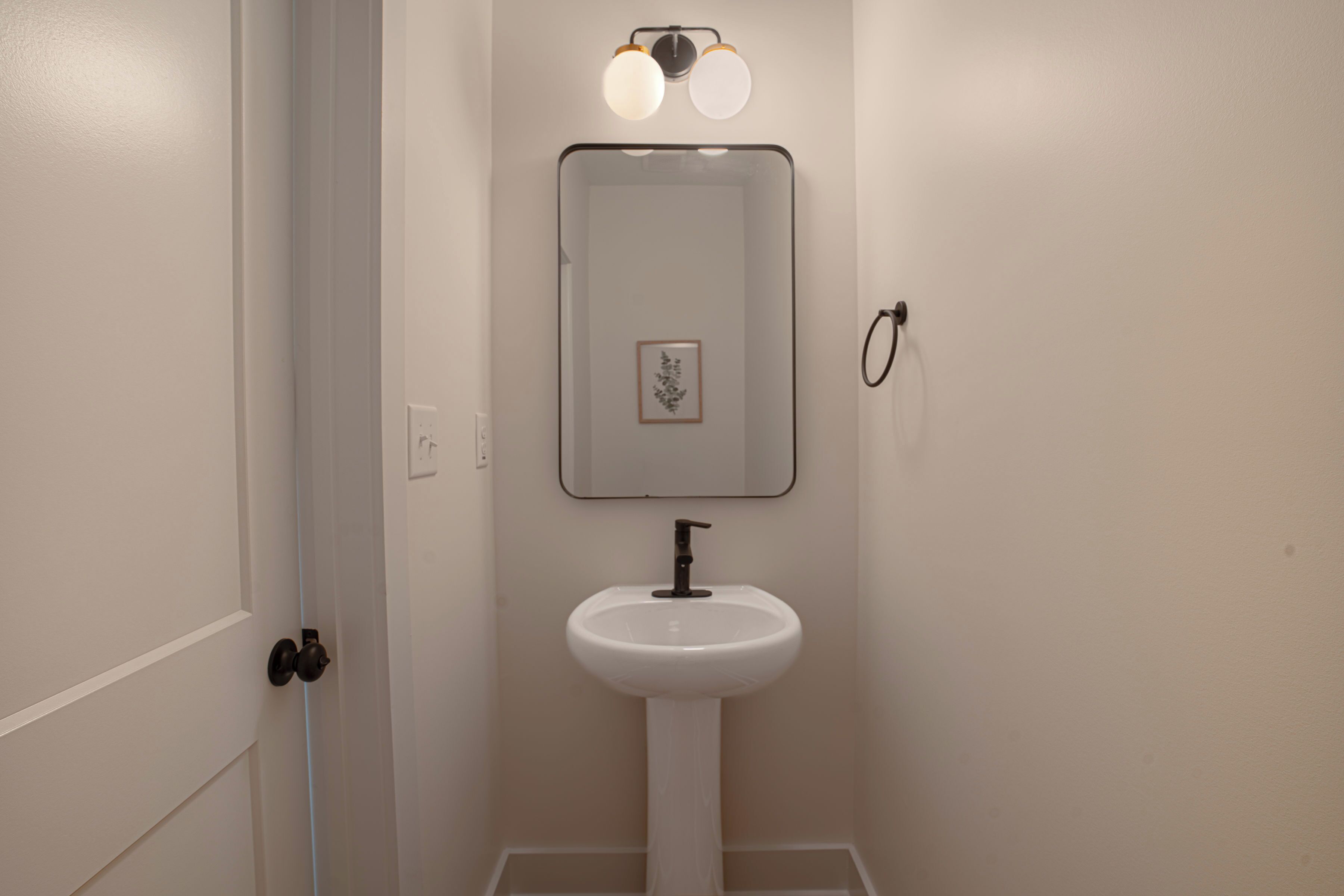 A bathroom with a white sink, a mirror, and a light fixture above the mirror.